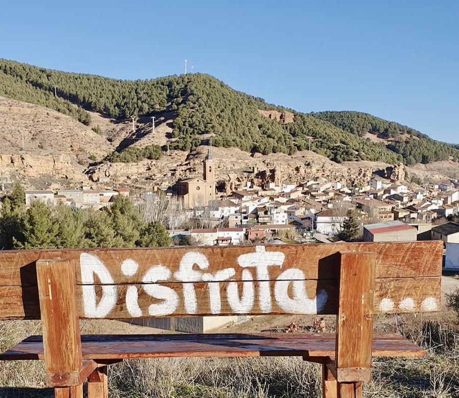 Banco de madera con la palabra Disfruta y vistas de Tosos al fondo
