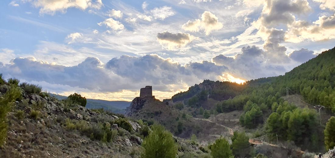El torreón de la Casaza coronando la peña al atardecer, con el sol poniéndose entre las nubes