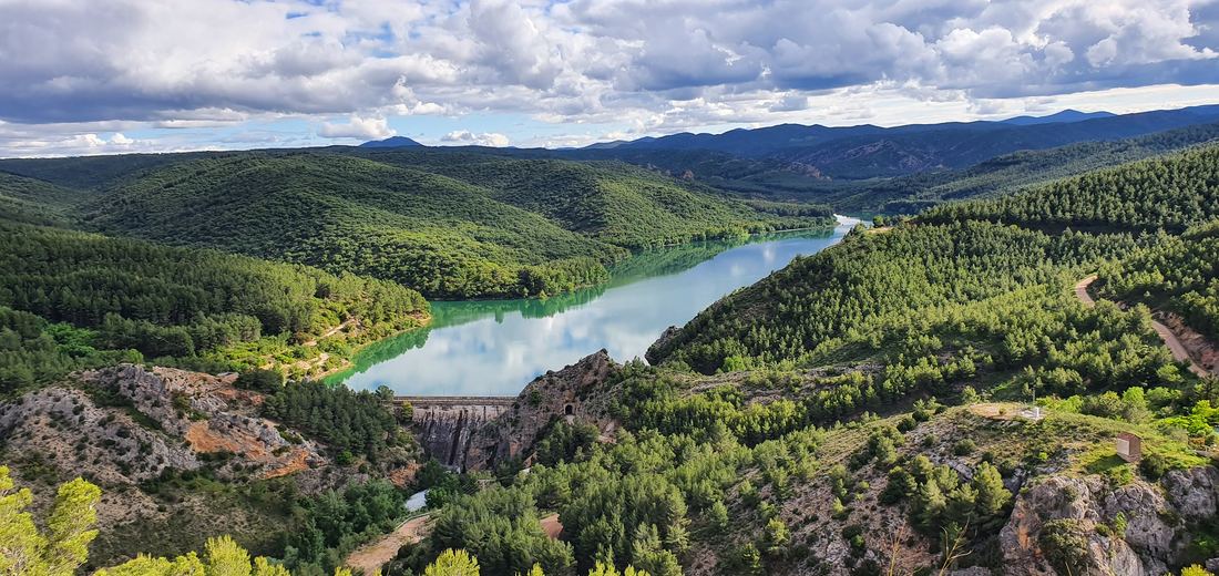 El embalse de Las Torcas con sus aguas turquesa quietas haciendo espejo, rodeado de pinares y montañas