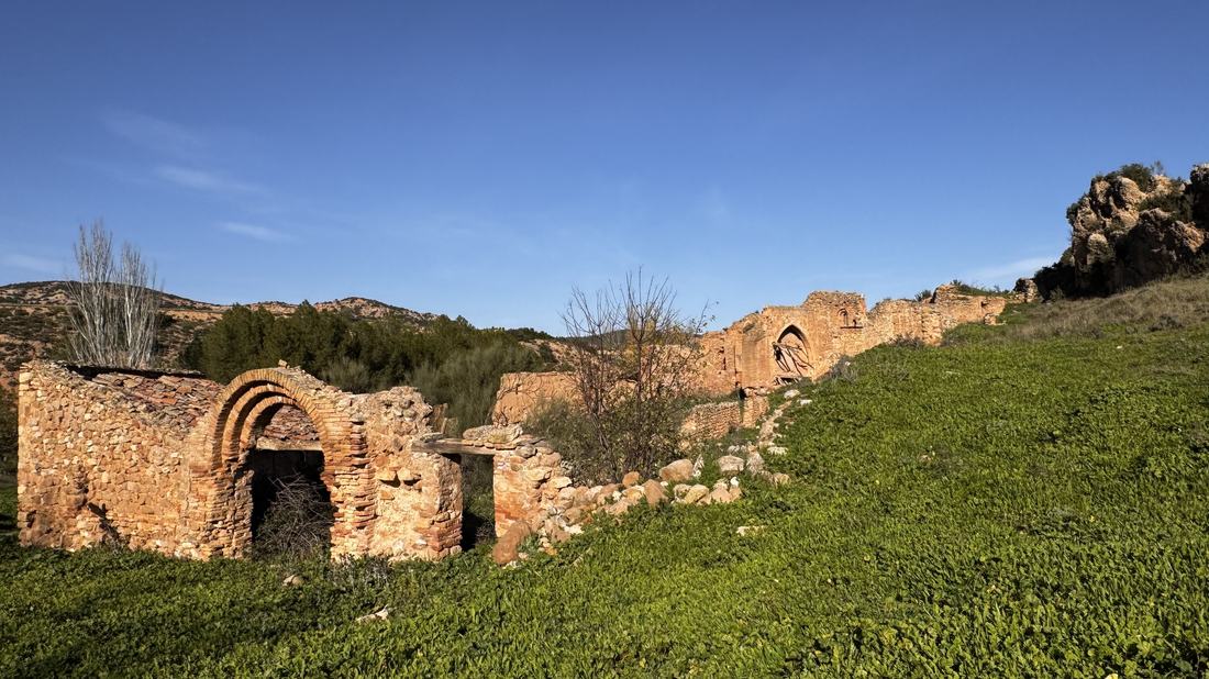 Vista general de las ruinas del Alcañicejo entre la hierba verde, con un arco de ladrillo en primer plano y los muros de la iglesia al fondo