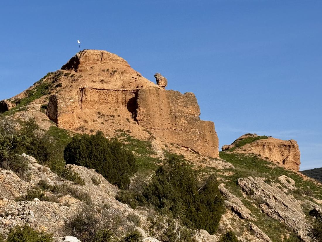Los restos del castillo musulmán sobre la peña rojiza que corona el Alcañicejo, con una bandera blanca en lo más alto