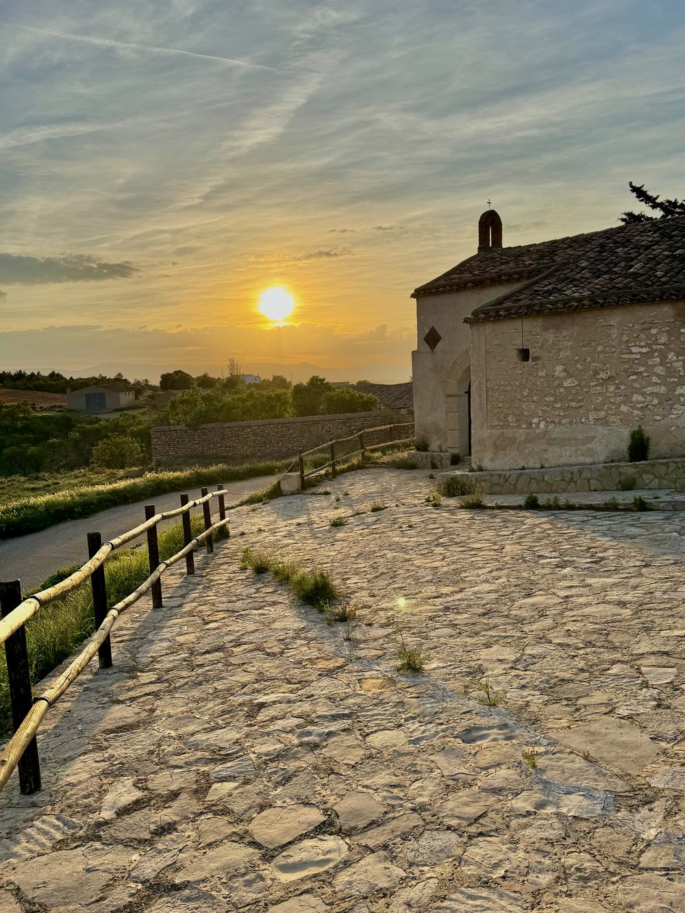La ermita de Santa Bárbara al atardecer, con el camino empedrado y el sol poniéndose sobre el valle